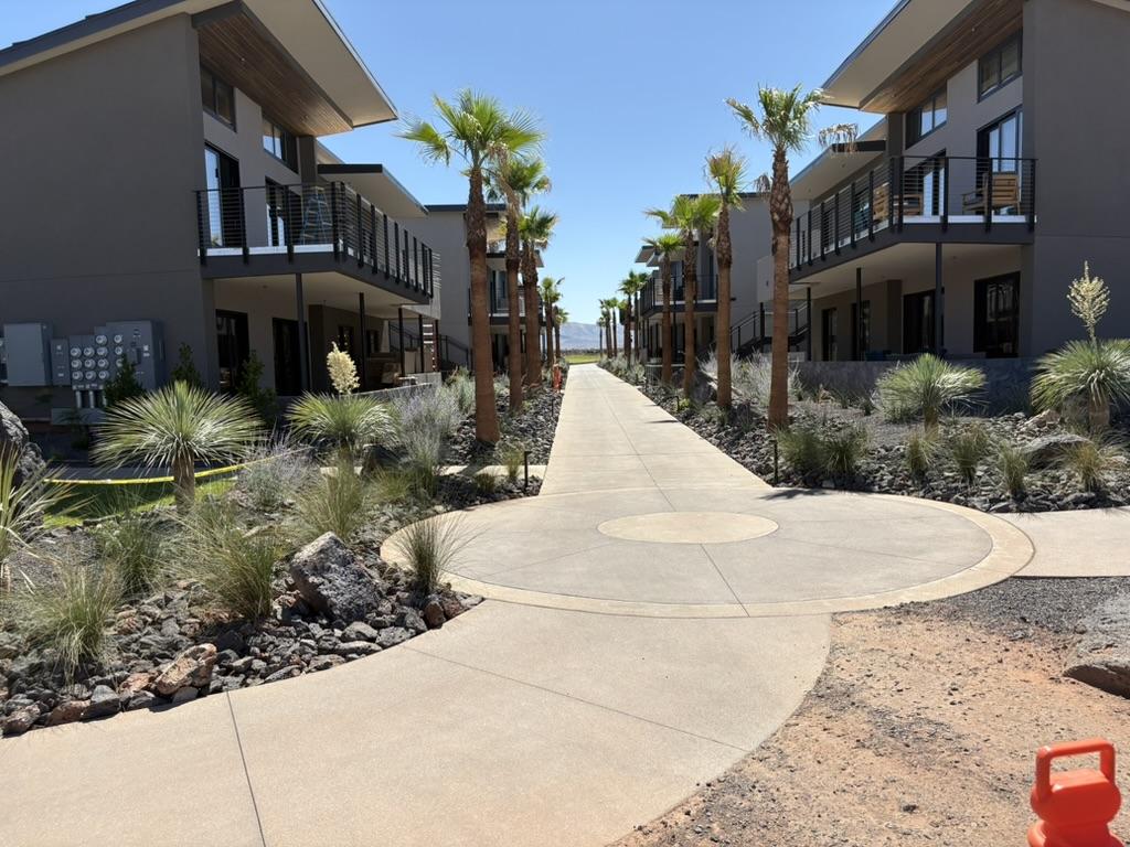 Commercial apartment walkway with concrete paths, palm trees, decorative rock landscaping, and modern multi level buildings
