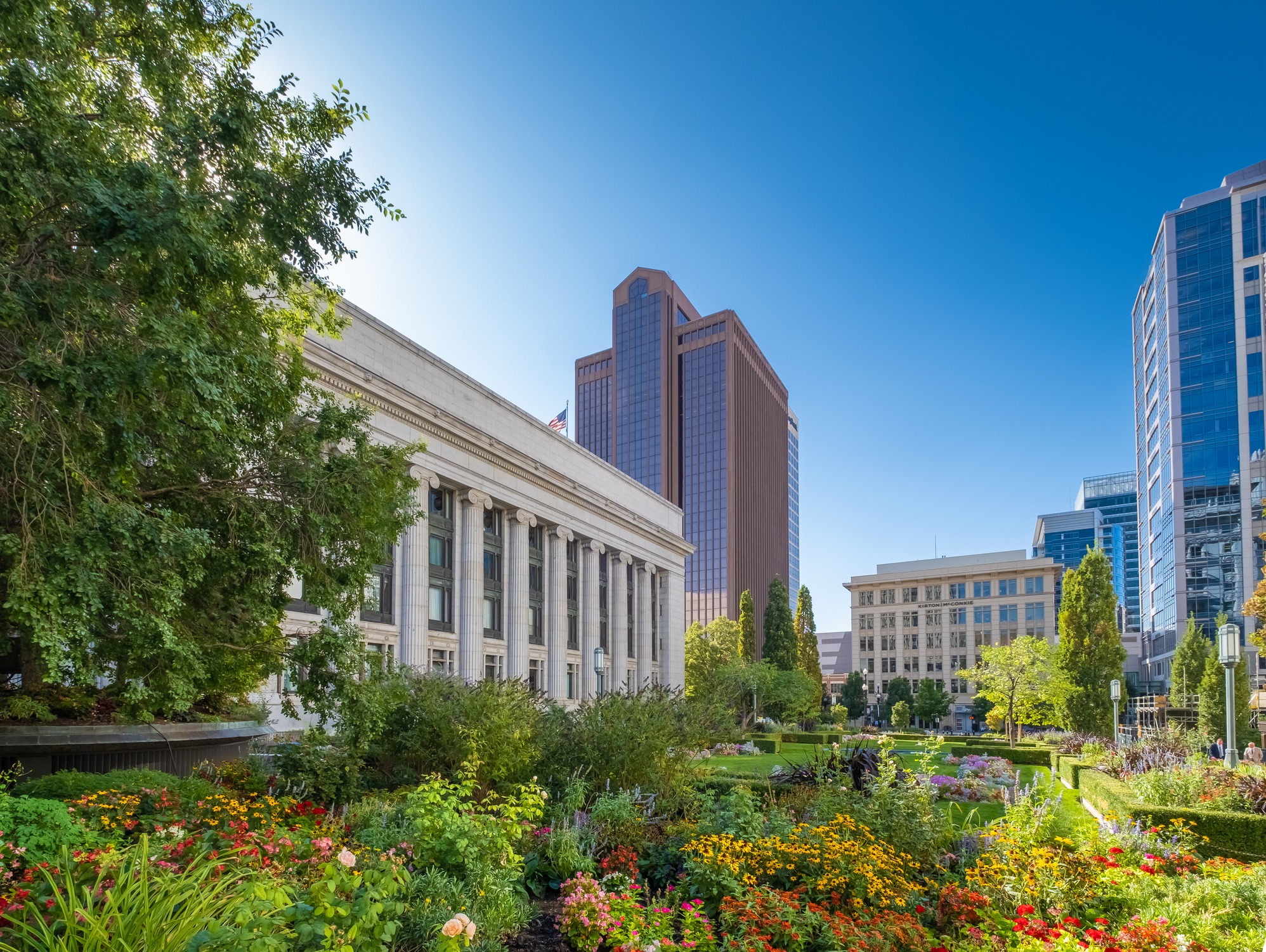 Urban garden with historic and modern buildings, sunny day.