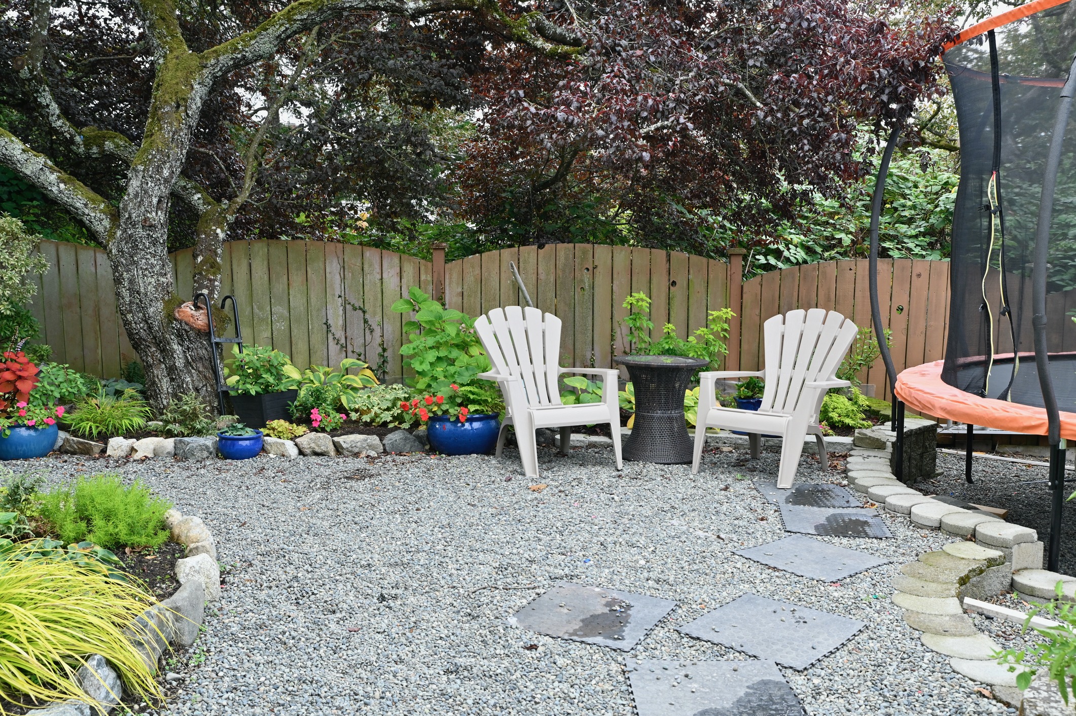 Backyard with chairs, plants, and trampoline